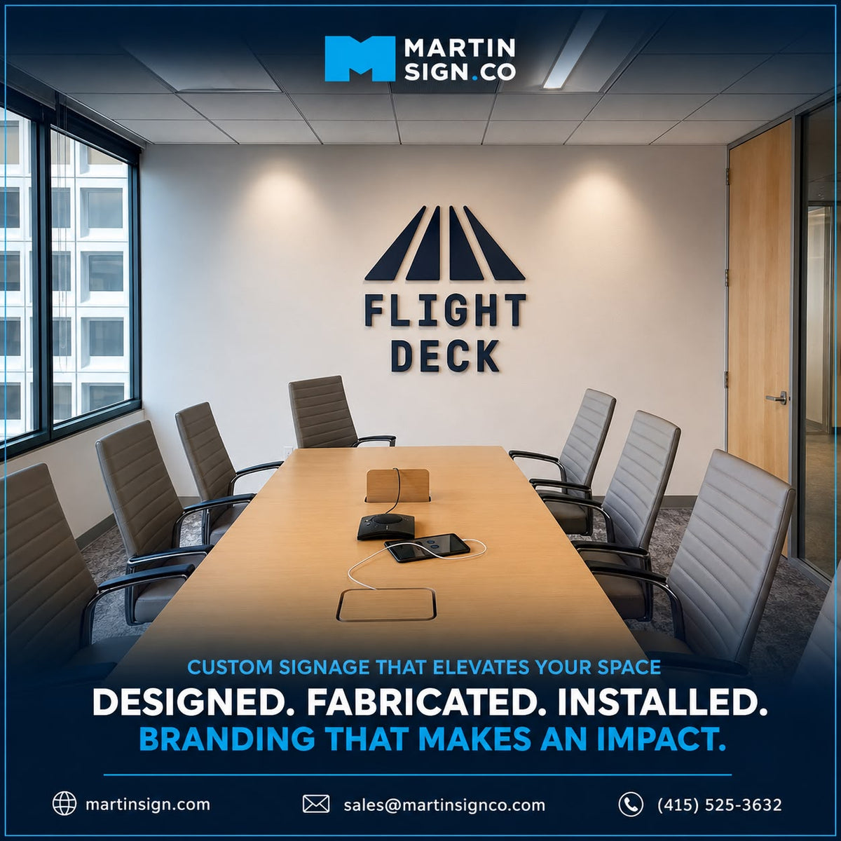 Custom corporate signage installed on a conference room wall, featuring the text 'FLIGHT DECK' beneath a stylized geometric logo. The room has a long wooden table, gray office chairs, and a modern ceiling.