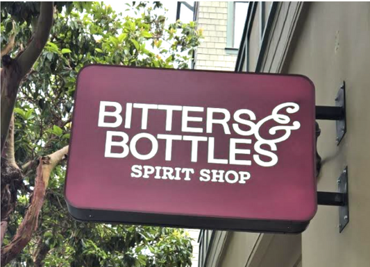 Sign for Bitters & Bottles Spirit Shop with trees and building in the background