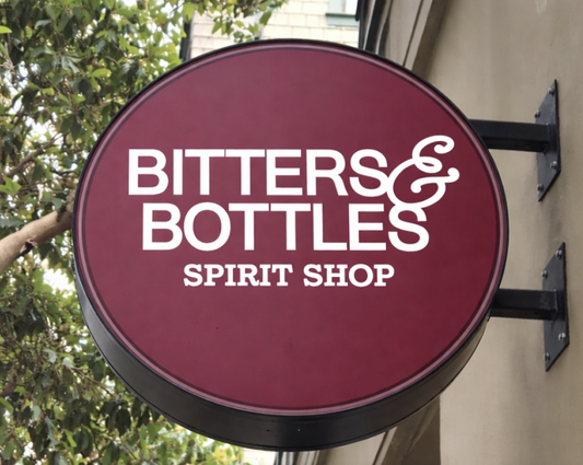 Round sign for Bitters & Bottles Spirit Shop with maroon background and white text.